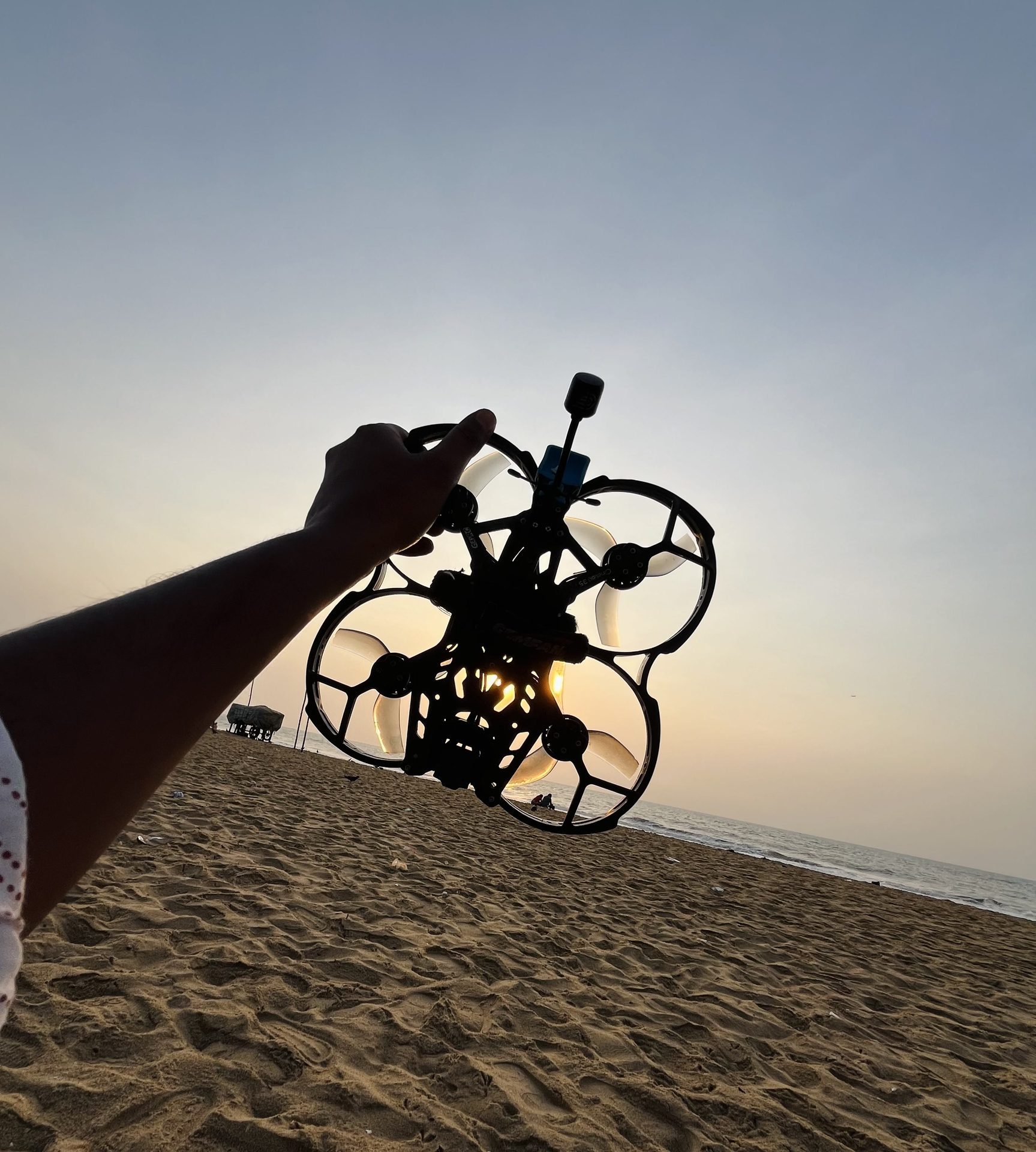 FPV whoop silhouetted against beach sunset